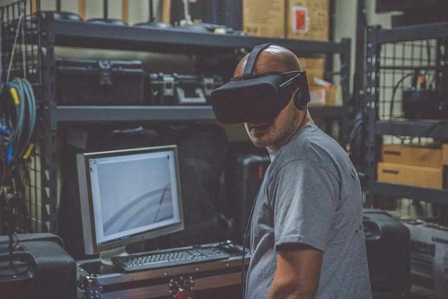 A person with headphones in a workshop with shelves and a computer monitor to play free paid PCVR games